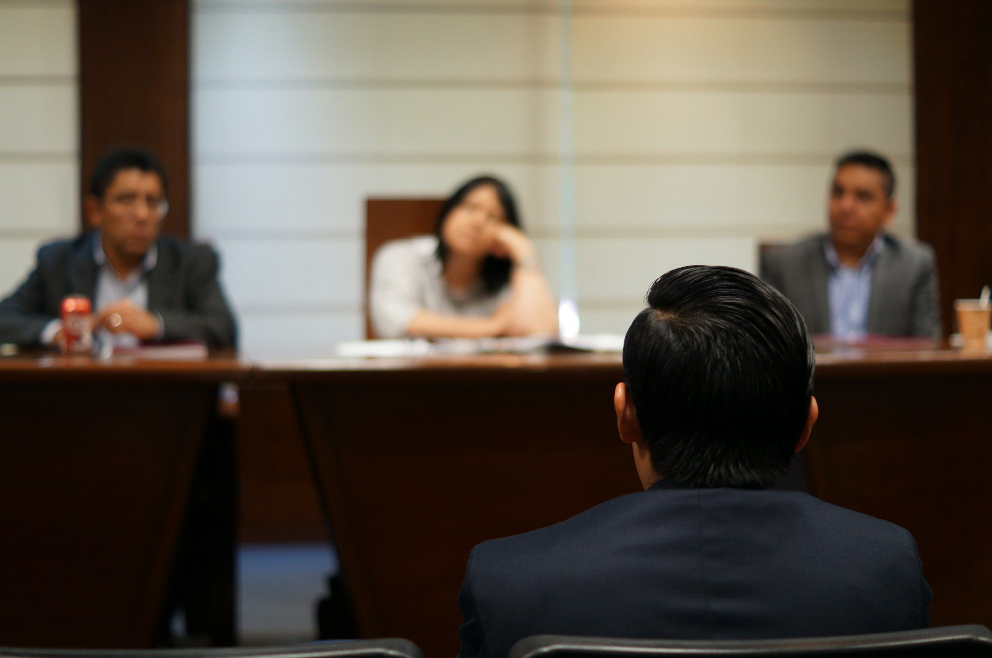 A person in a suit facing three people seated at a long wooden table